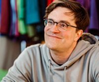 Ein Mann mit Brille im Kapuzenpullover lächelt freundlich in die Kamera