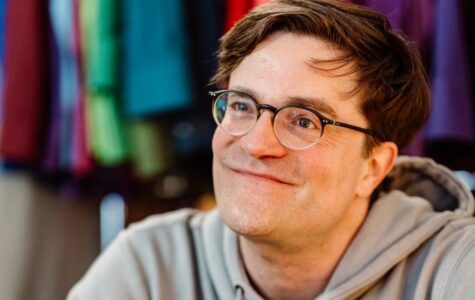 Ein Mann mit Brille im Kapuzenpullover lächelt freundlich in die Kamera