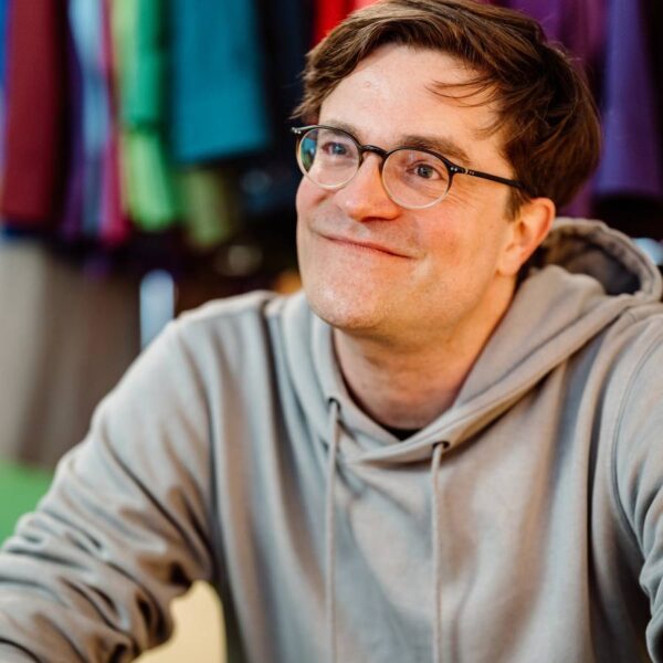 Ein Mann mit Brille im Kapuzenpullover lächelt freundlich in die Kamera