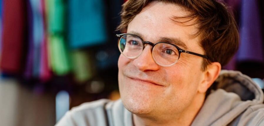 Ein Mann mit Brille im Kapuzenpullover lächelt freundlich in die Kamera