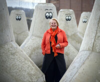 Eine lachende Frau steht zwischen riesigen Betonpollern mit aufgemalten Augen