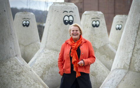 Eine lachende Frau steht zwischen riesigen Betonpollern mit aufgemalten Augen