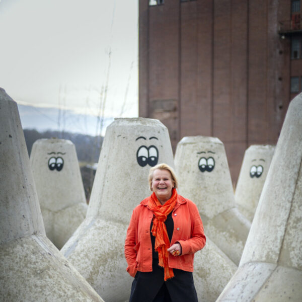 Eine lachende Frau steht zwischen riesigen Betonpollern mit aufgemalten Augen