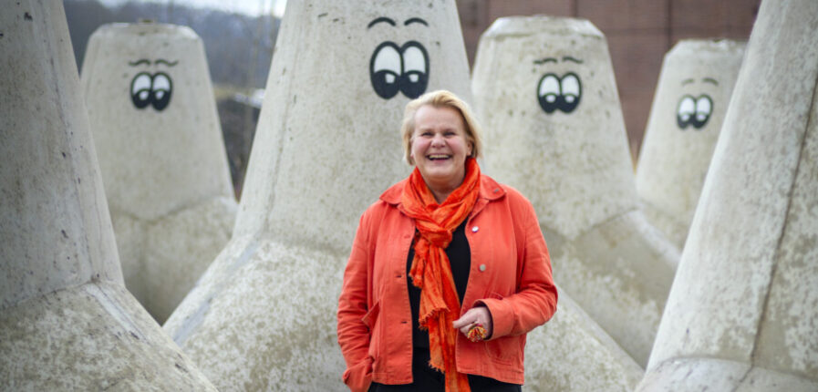 Eine lachende Frau steht zwischen riesigen Betonpollern mit aufgemalten Augen
