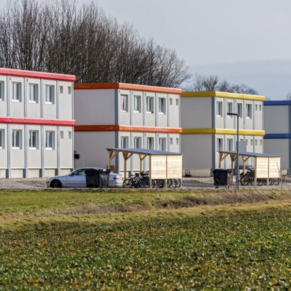 Drei Gebäude aus gestapelten grau-blauen Containern, davor Fahrräder und ein Auto