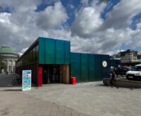 Das gläserne Gebäude der Hamburger Bahnhofsmission unter bewölktem Himmel.