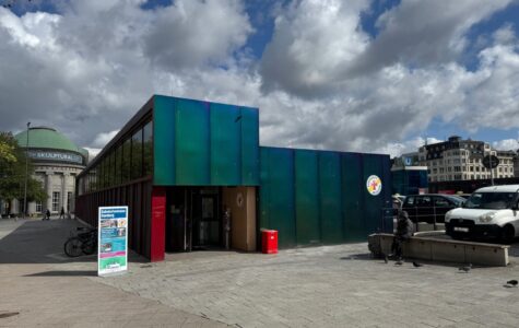 Das gläserne Gebäude der Hamburger Bahnhofsmission unter bewölktem Himmel.