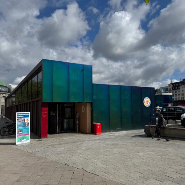 Das gläserne Gebäude der Hamburger Bahnhofsmission unter bewölktem Himmel.
