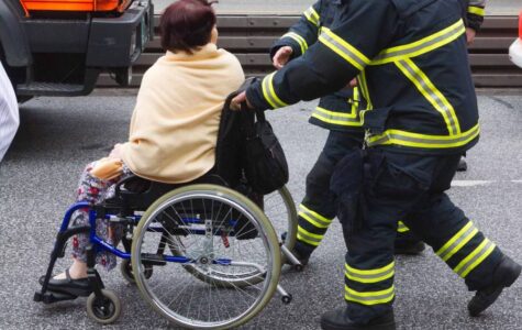 Eine Frau im Rollstuhl wird von zwei Feuerwehrleuten geschoben