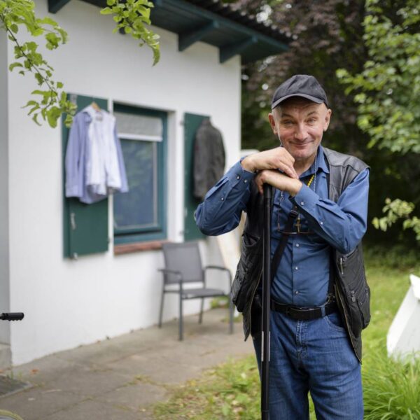 Ein Mann steht vor einem kleinen Haus und schaut freundlich in die Kamera