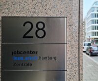 Ein Türschild mit der Aufschrift "jobcenter team.arbeit.hamburg Zentrale"
