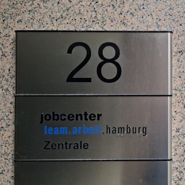 Ein Türschild mit der Aufschrift "jobcenter team.arbeit.hamburg Zentrale"