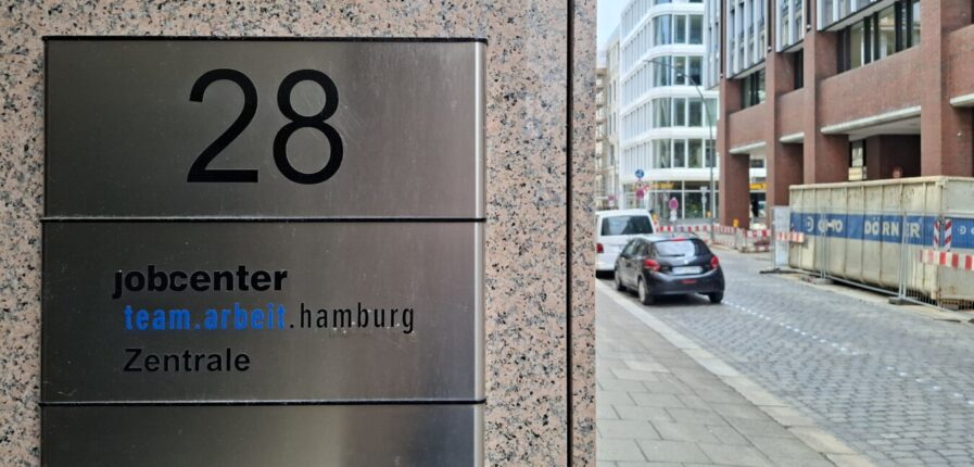 Ein Türschild mit der Aufschrift "jobcenter team.arbeit.hamburg Zentrale"