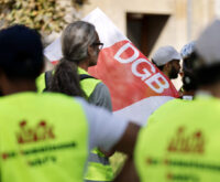 Menschen in gelben Warnwesten vor einer DGB-Fahne