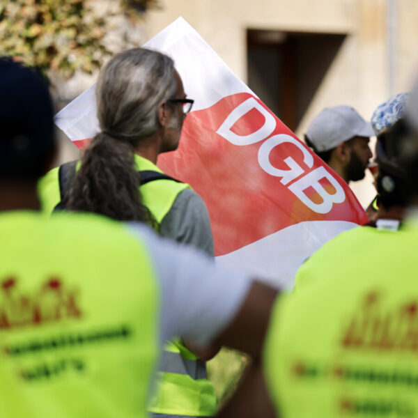 Menschen in gelben Warnwesten vor einer DGB-Fahne