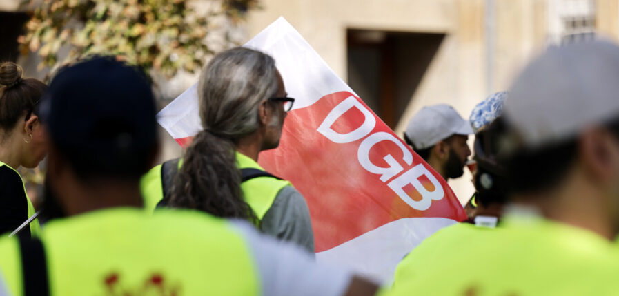 Menschen in gelben Warnwesten vor einer DGB-Fahne