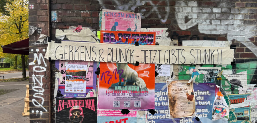 An einer Hauswand hängen viele Plakate. Quer darüber hängt ein Banner mit der Aufschrift: "Gerkens & Blunck – Jetzt gibt's Stunk"
