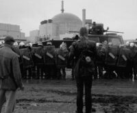 Im Hintergrund ein Atom-Meiler, davor eine Polizeikette