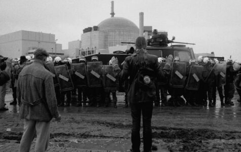Im Hintergrund ein Atom-Meiler, davor eine Polizeikette