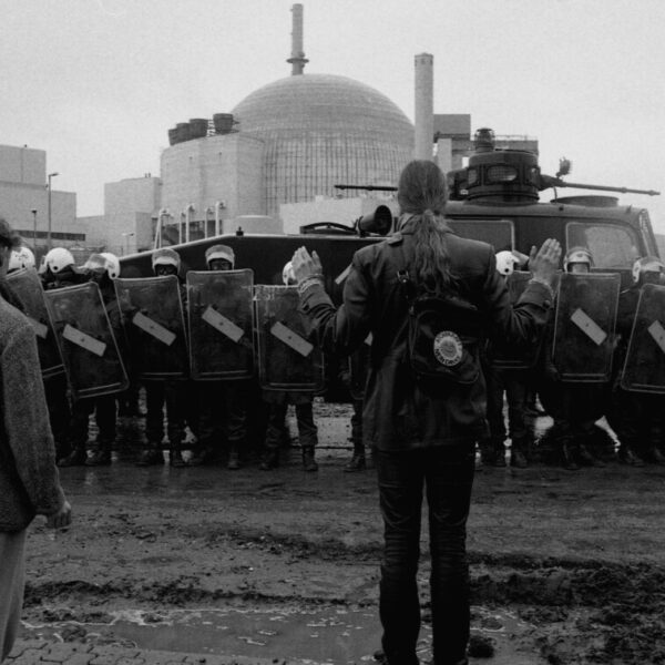 Im Hintergrund ein Atom-Meiler, davor eine Polizeikette