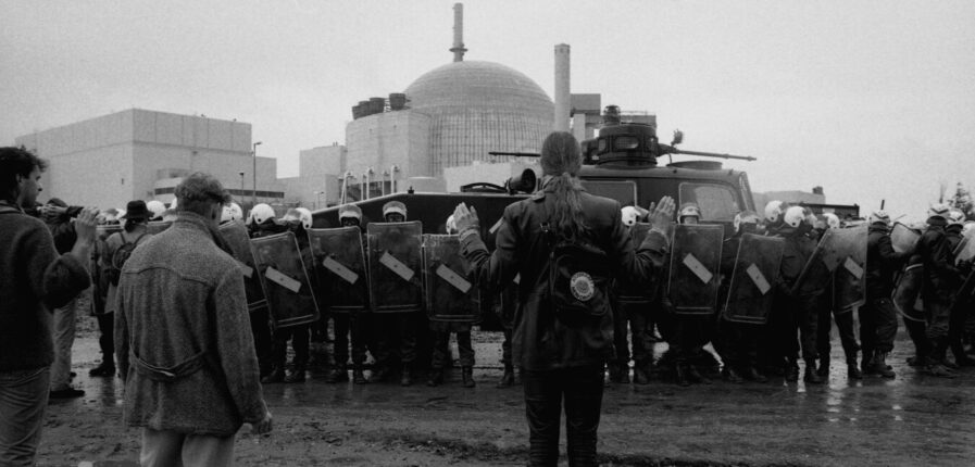 Im Hintergrund ein Atom-Meiler, davor eine Polizeikette