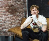 Malte Zierden sitzt auf einem beigen Sofa und lächelt freundlich in die Kamera.