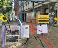 Ein Bauzaun mit angehefteten Fotos von einem Mann, dazu Schriftzüge wie "Rest in Peace Ahmed"