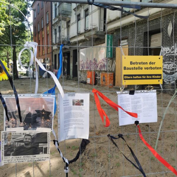 Ein Bauzaun mit angehefteten Fotos von einem Mann, dazu Schriftzüge wie "Rest in Peace Ahmed"