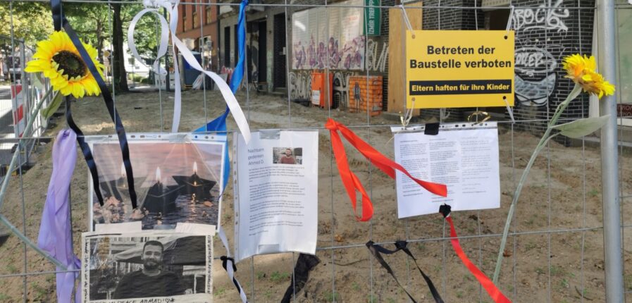 Ein Bauzaun mit angehefteten Fotos von einem Mann, dazu Schriftzüge wie "Rest in Peace Ahmed"